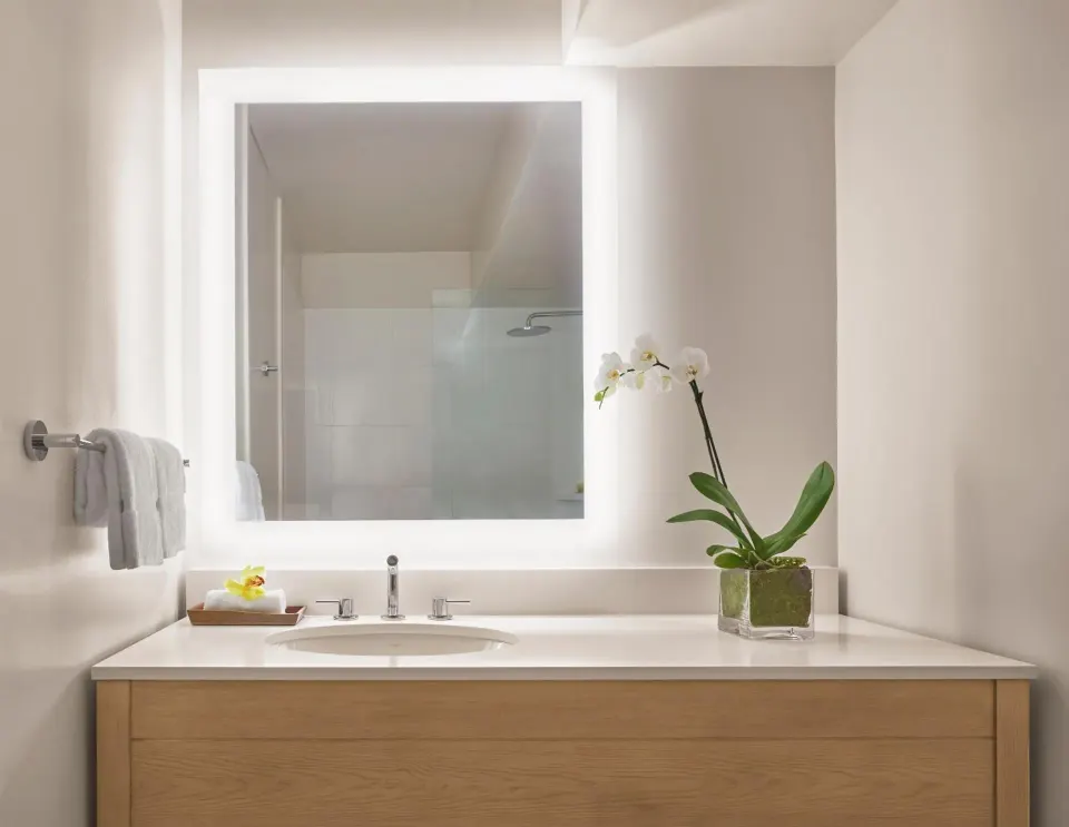 Bathroom vanity with lit mirror in a Classic 2 Queens room at 'Alohilani Resort Waikiki Beach.