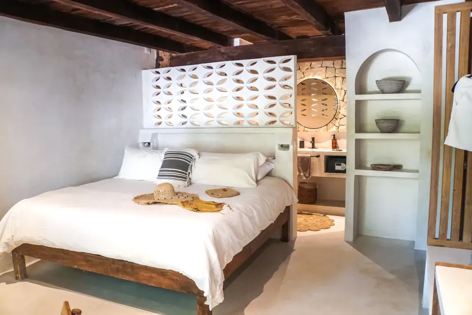 White-dressed bed with patterned pillow and open bathroom niche at Amansala