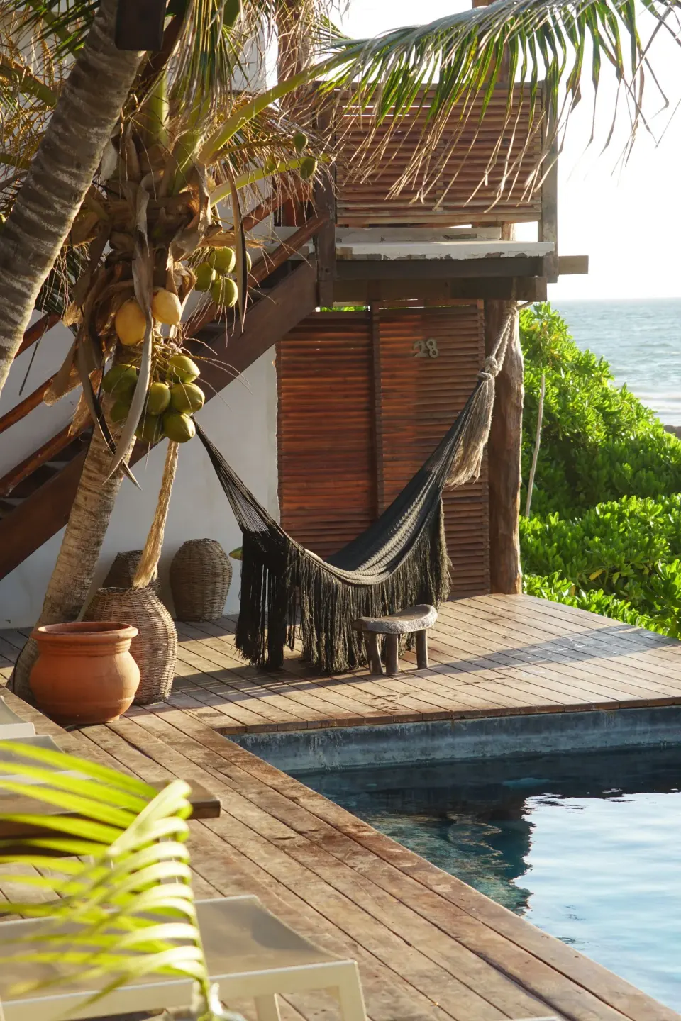 Black hammock on a wooden deck next to a pool and coconut palm at Amansala