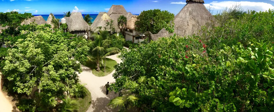 Lush resort grounds with pathways, thatched rooftops and ocean visible beyond at Amansala