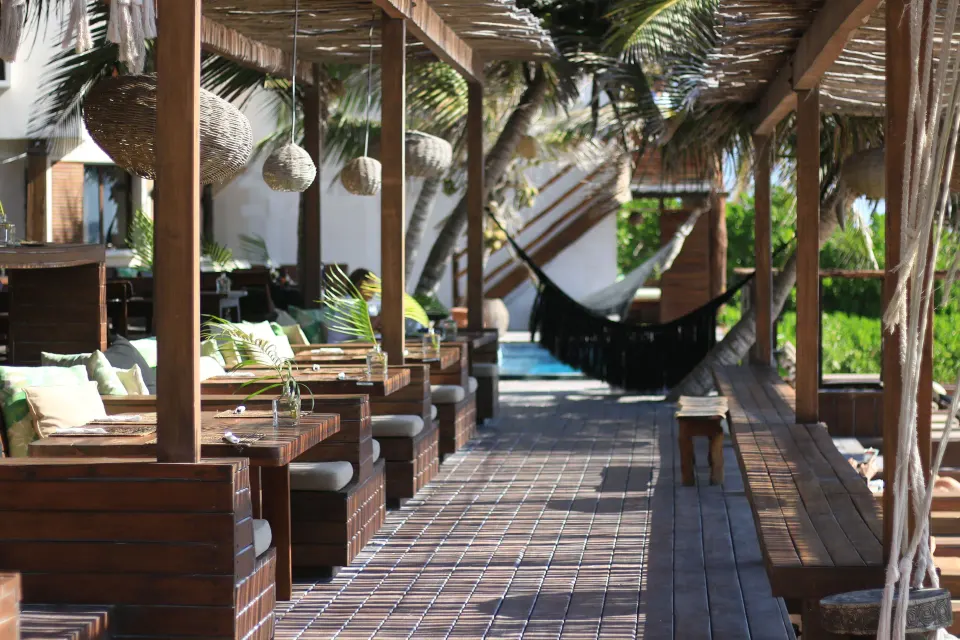Covered wooden dining booths and a black hammock along a beachfront deck at Amansala