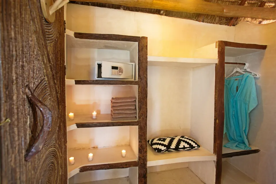 Built-in shelving and open closet with safe and hanging robe in a simple room at Amansala