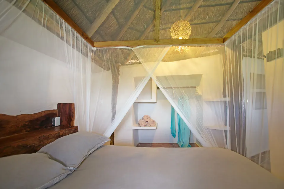 King bed with mosquito net and thatched ceiling in a simple room at Amansala