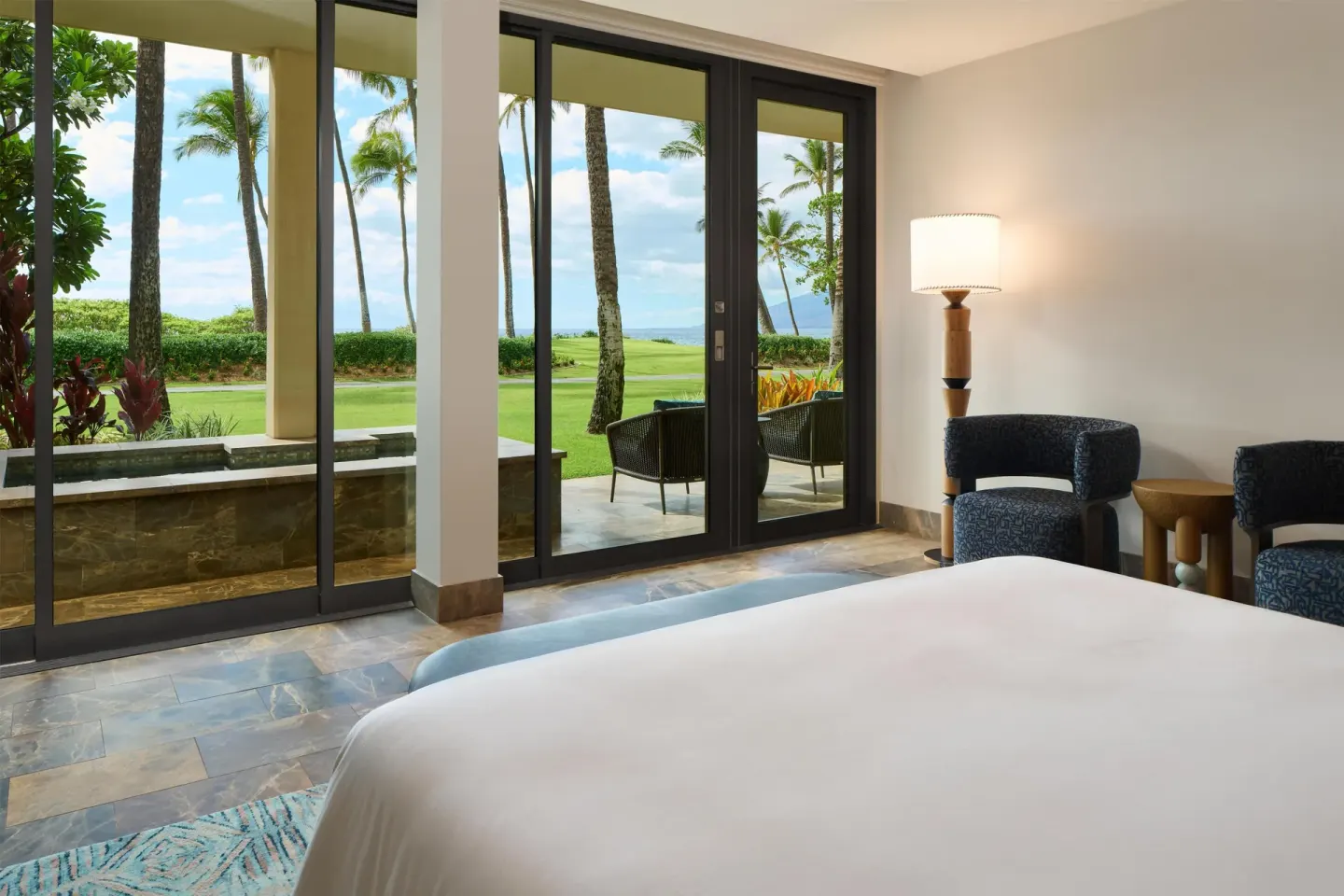 Guest room bed and patio doors with palm lawn views at Andaz Maui at Wailea Resort.