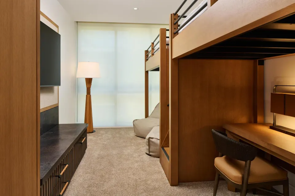 Bunk room with desk, wall TV, and lounge chair in a villa at Andaz Maui at Wailea Resort.