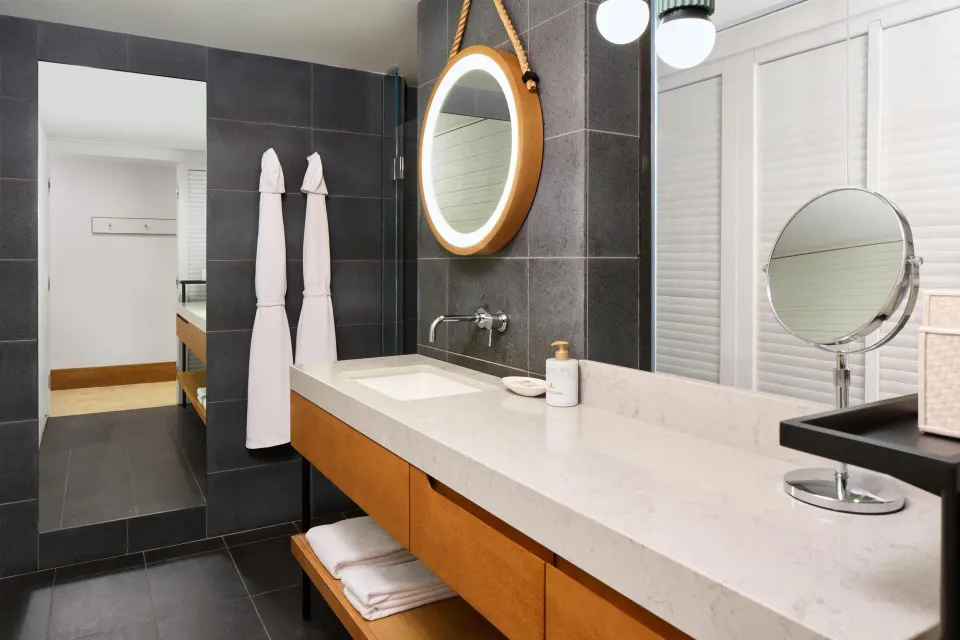 Guest room bathroom vanity with round mirror and robes at Andaz Maui at Wailea Resort.