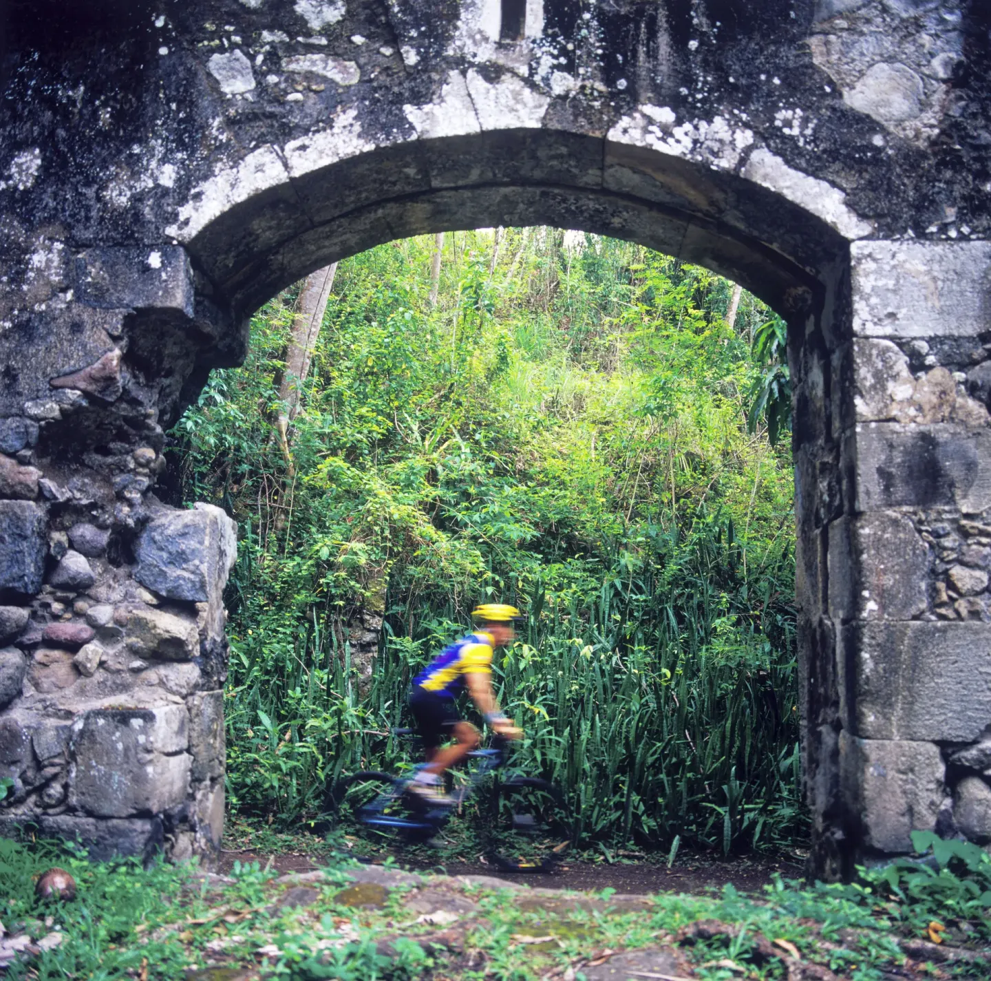 A cyclist rides through a weathered stone arch in the forest at Anse Chastanet Resort.