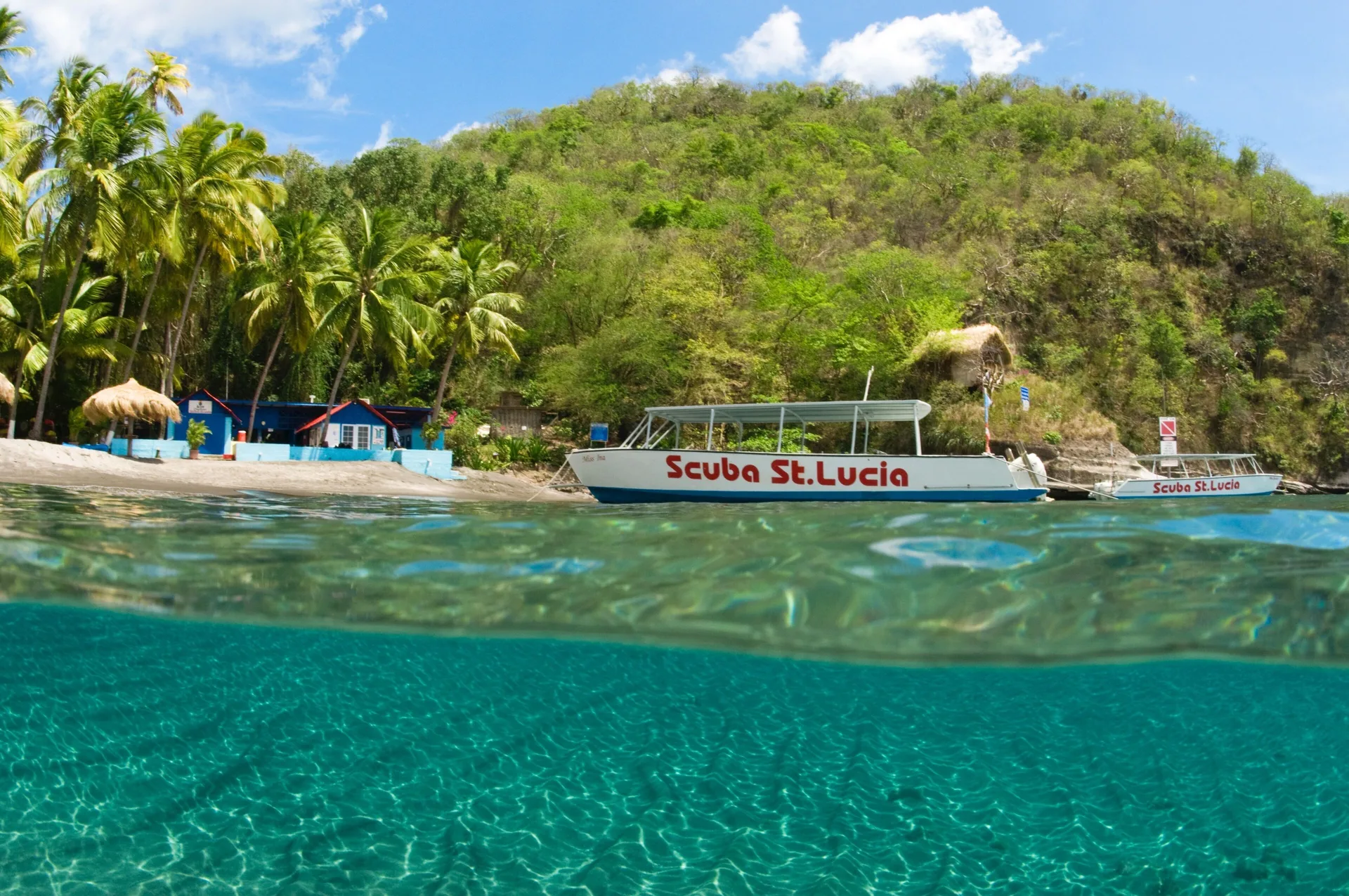 Dive boats float by the beach in clear water at Anse Chastanet Resort.