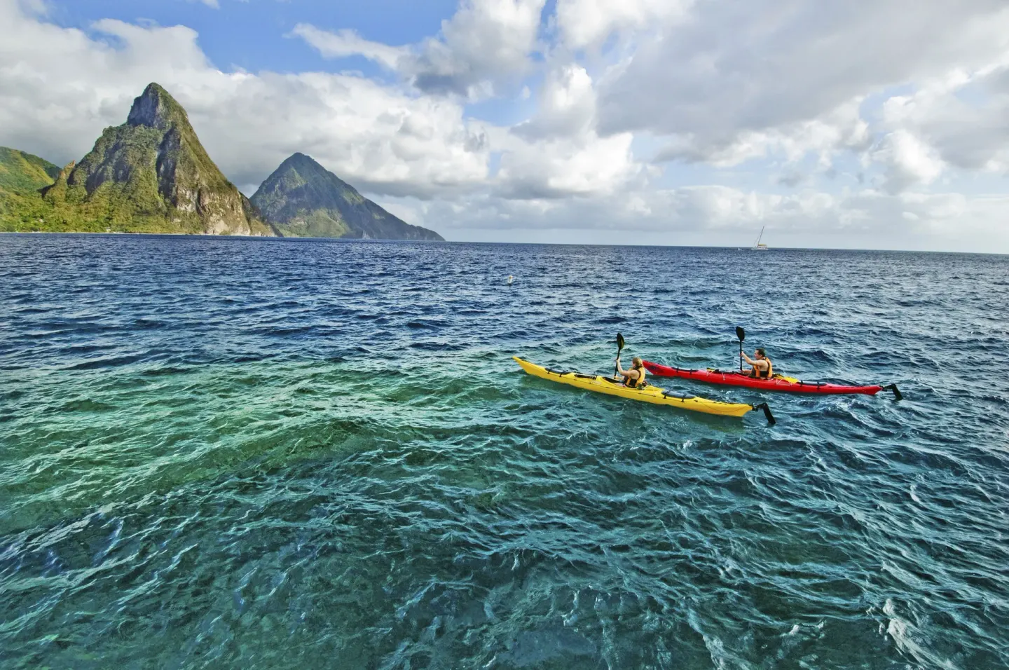 Kayakers paddle on clear water with the Pitons beyond Anse Chastanet Resort.