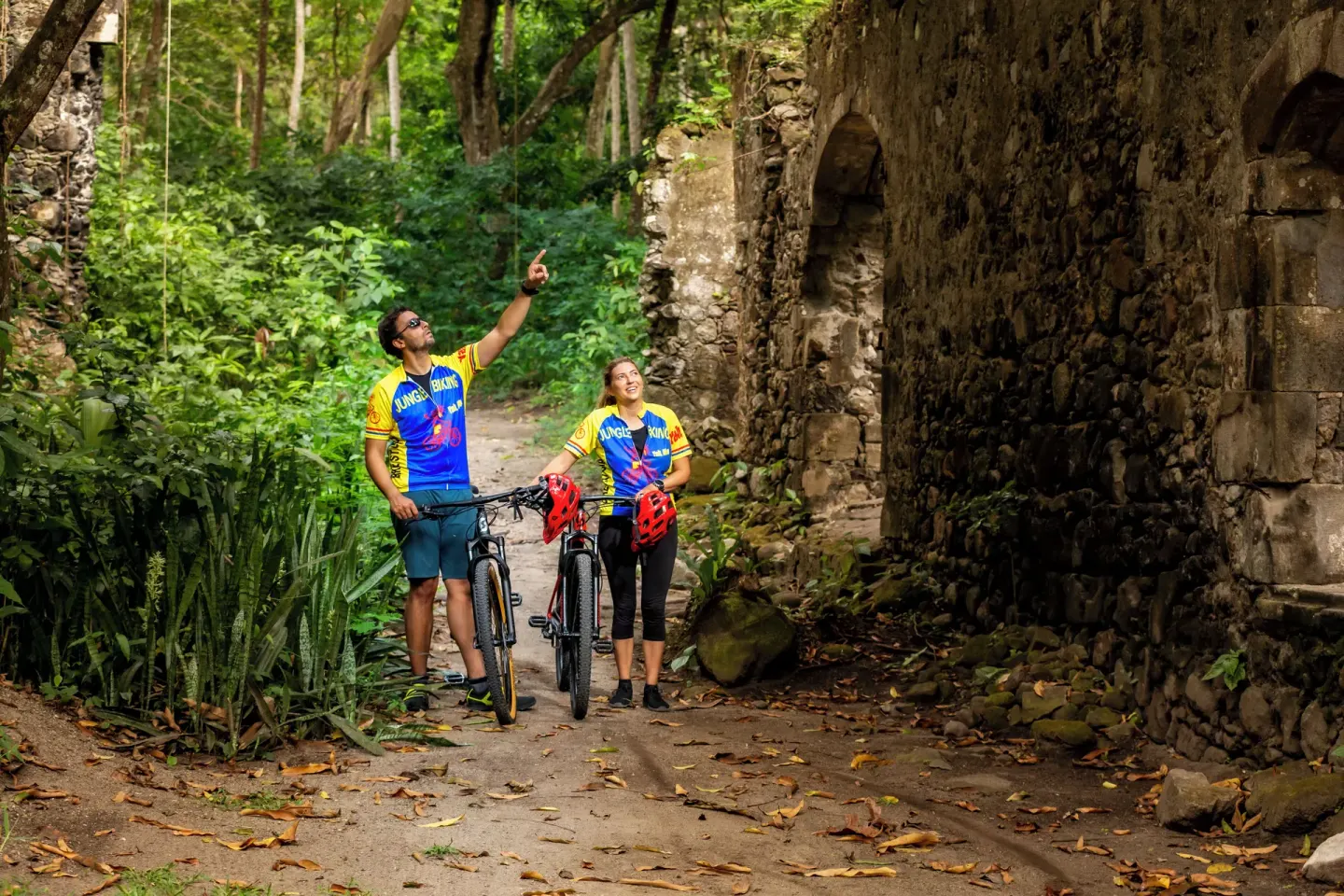 Cyclists with mountain bikes beside old stone ruins at Anse Chastanet Resort.