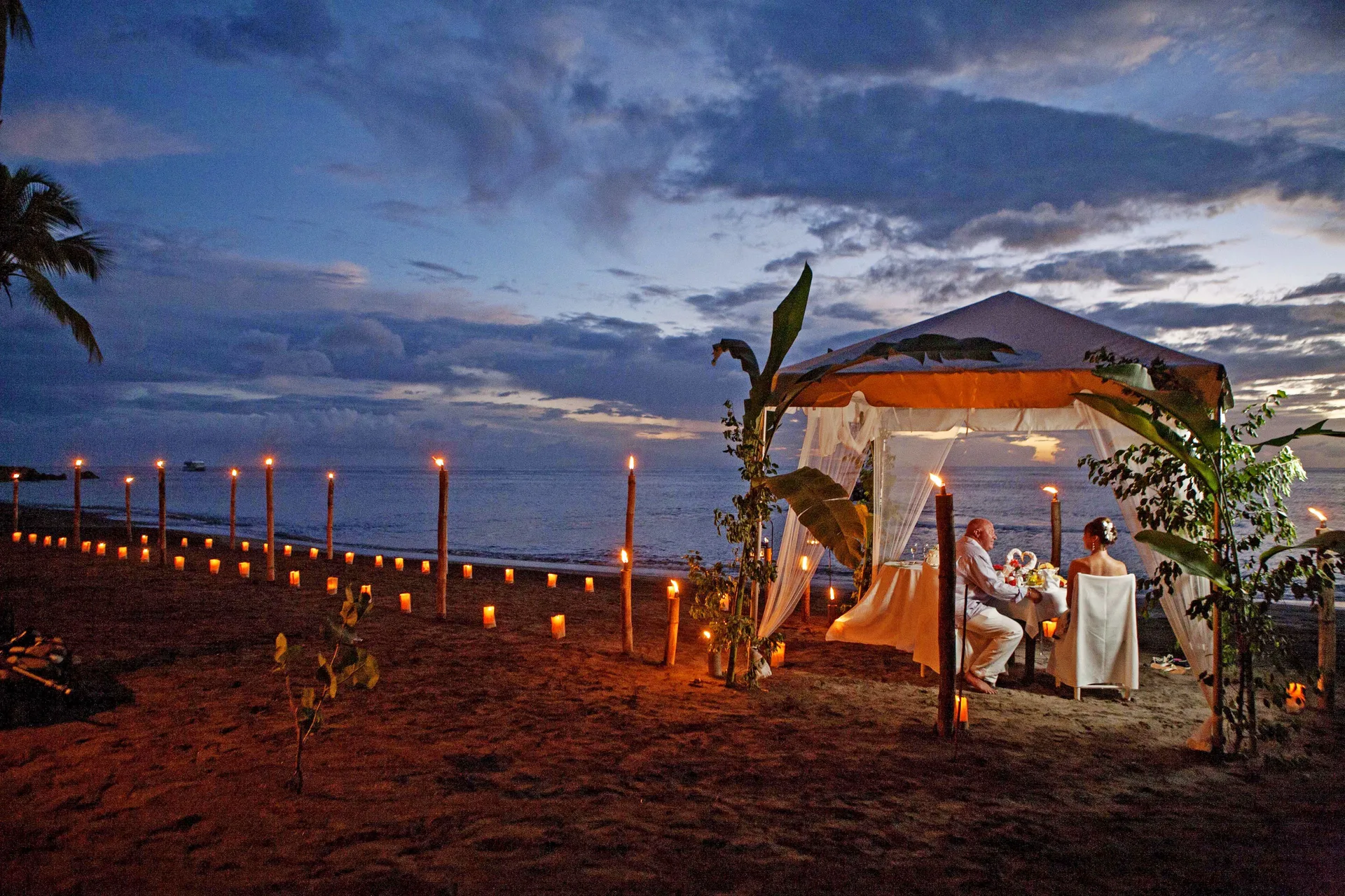 Couple dining in a candlelit beach cabana at dusk at Anse Chastanet Resort.