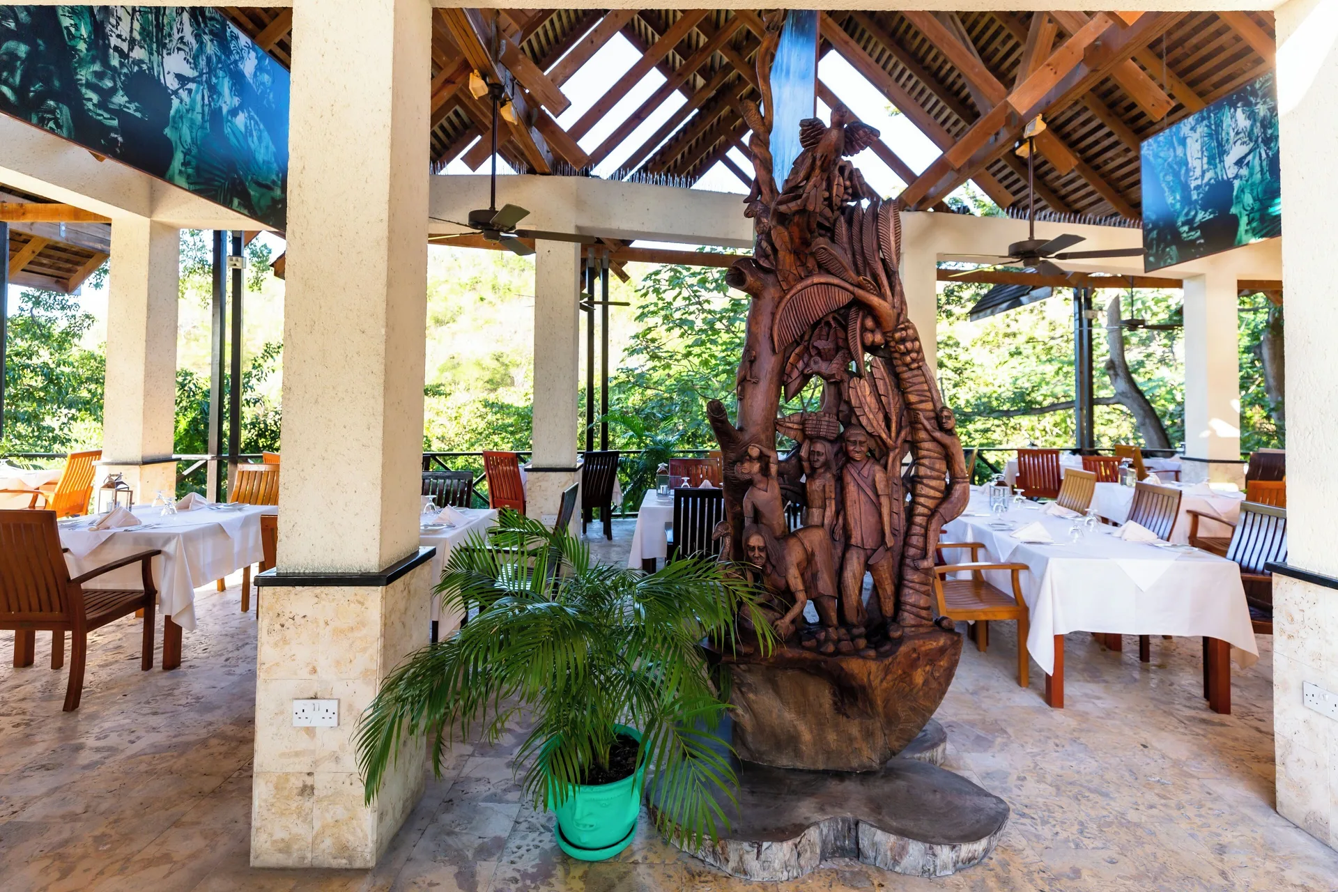 Open-air dining room with white tablecloths and a carved sculpture at Anse Chastanet Resort.