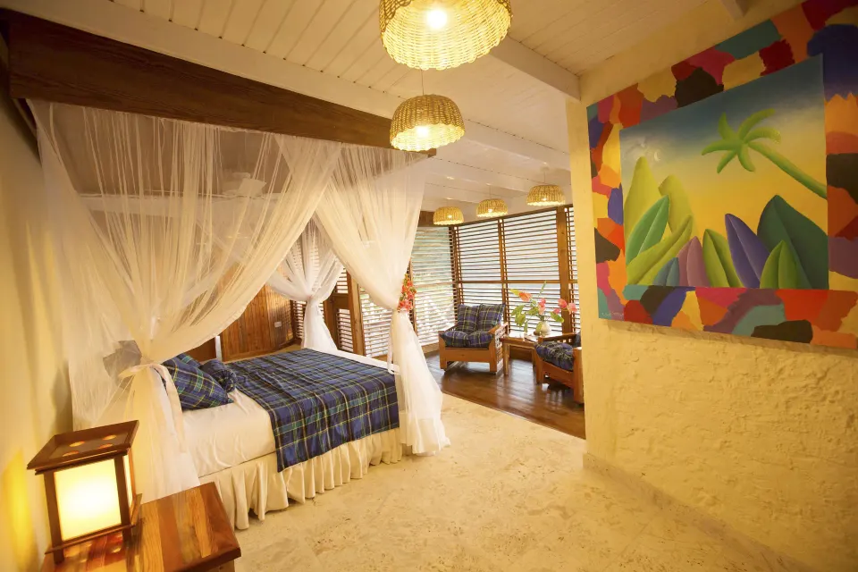 Standard Room with netted bed, tropical wall art and louvered sitting area at Anse Chastanet Resort.