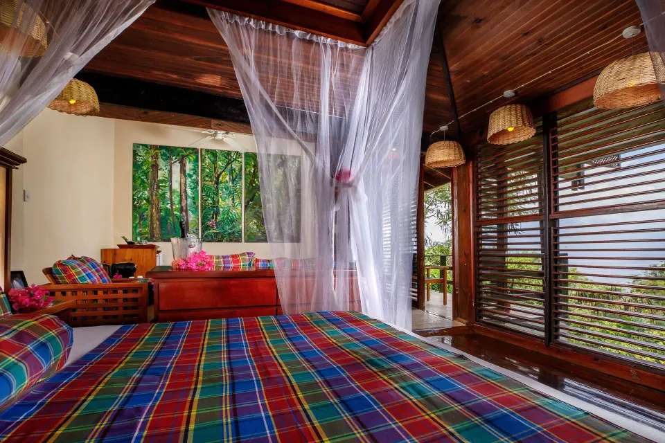 Standard Room bed with plaid linens, mosquito netting and shuttered sea-facing opening at Anse Chastanet Resort.