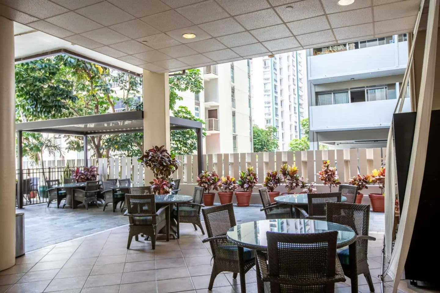 Covered patio seating with round tables and potted plants at Aqua Aloha Surf Waikiki.
