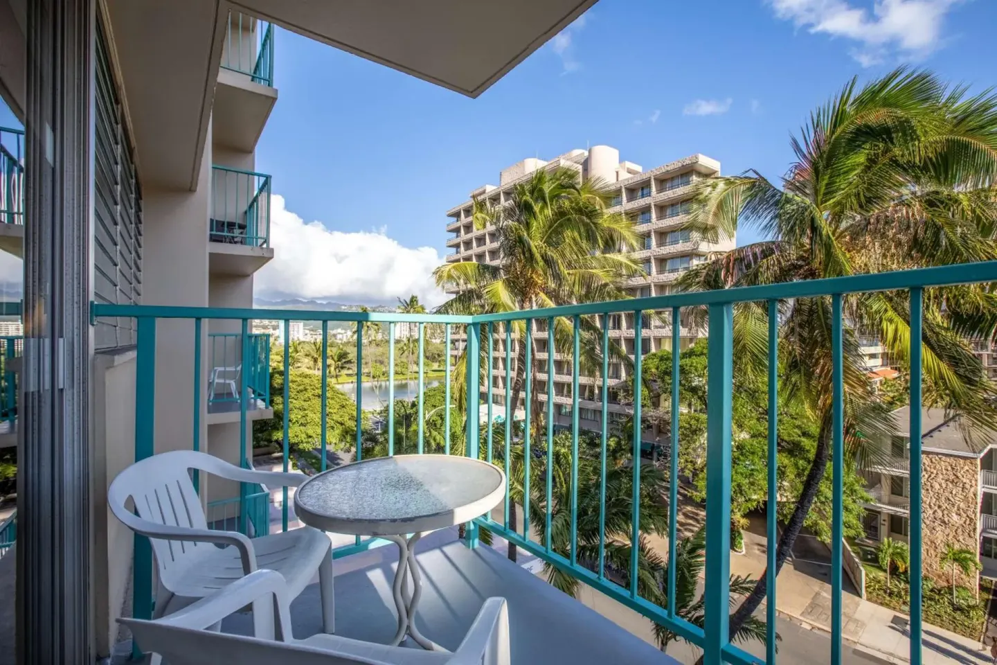 Guest balcony with table, chairs, palms, and city view at Aqua Aloha Surf Waikiki.