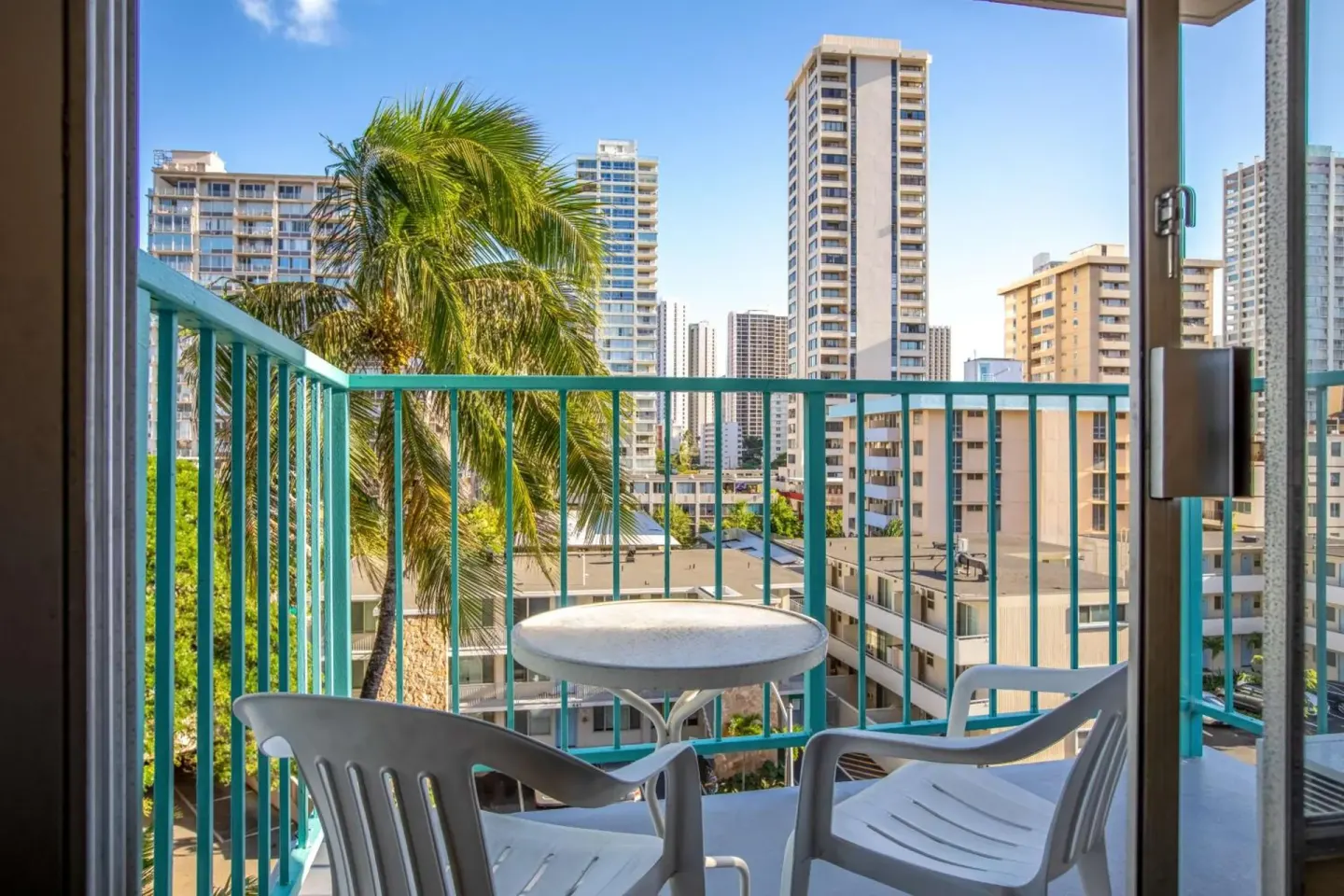 Balcony with chairs, table, palm tree, and city towers at Aqua Aloha Surf Waikiki.