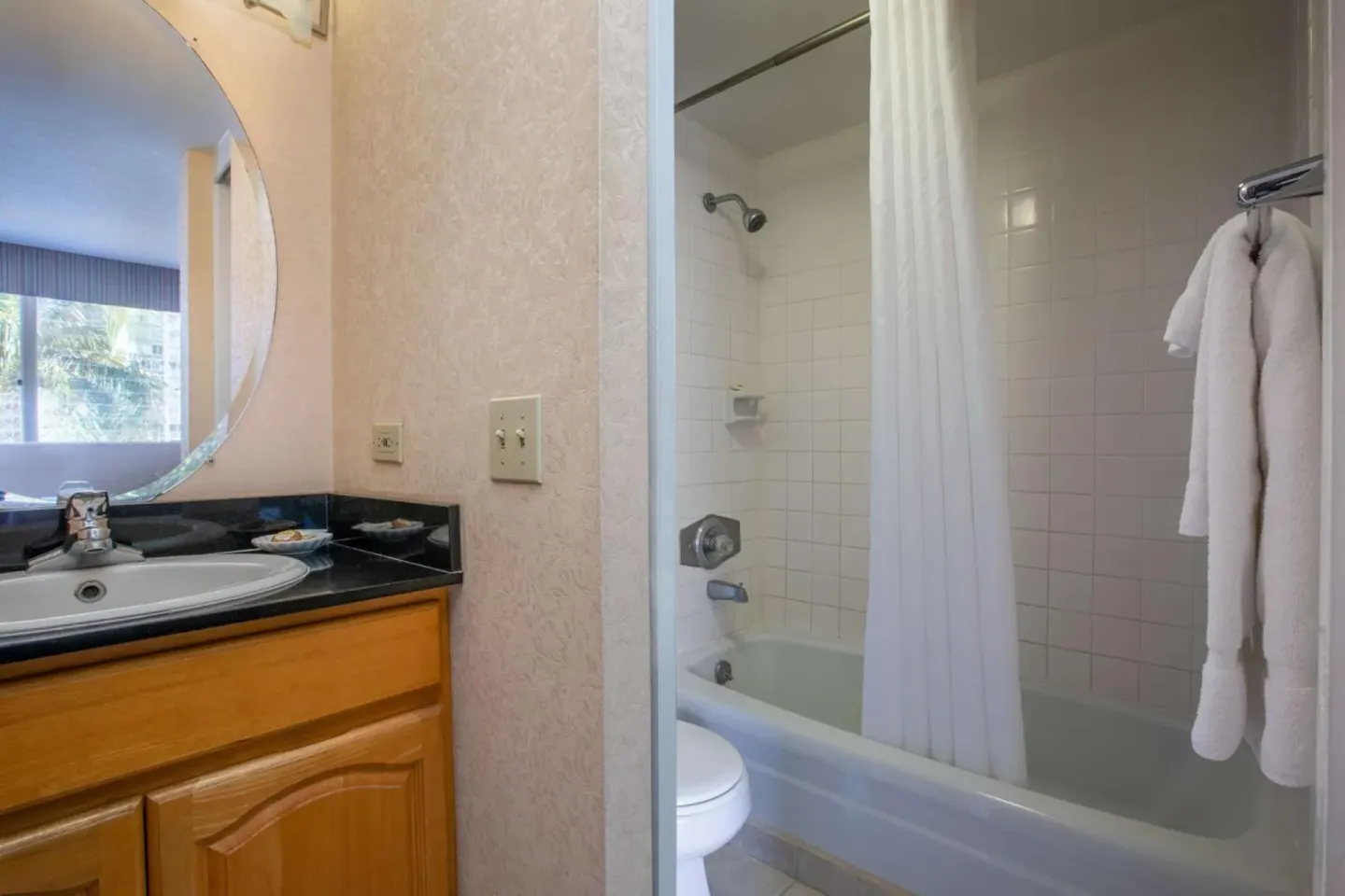 Bathroom with vanity, tub-shower, curtain, and robes at Aqua Aloha Surf Waikiki.