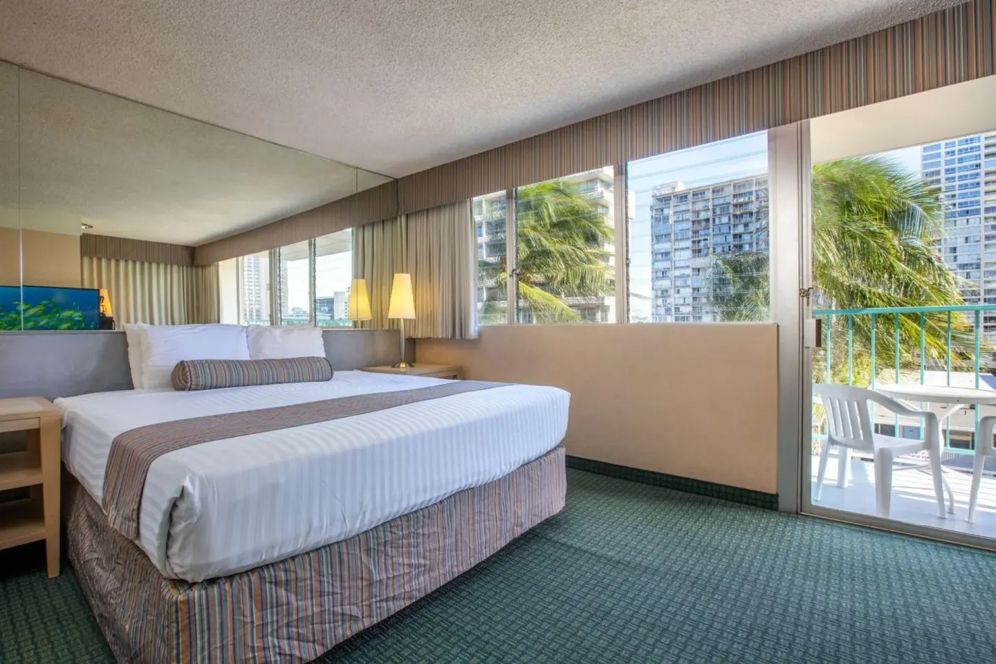 Guest room with king bed, large windows, and balcony seating at Aqua Aloha Surf Waikiki.
