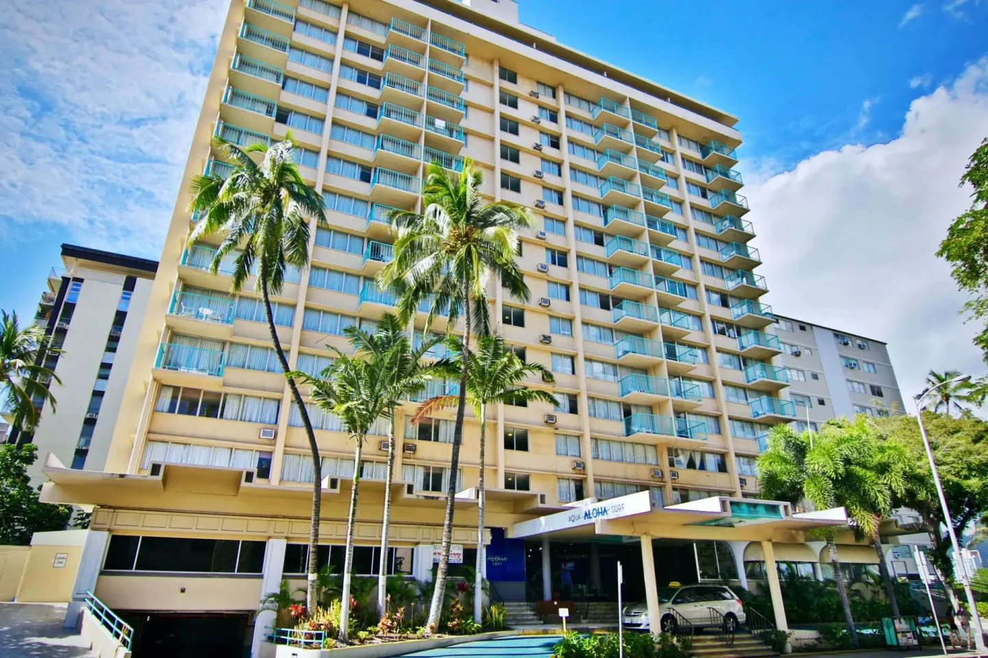Tall hotel exterior with balconies and palm trees at Aqua Aloha Surf Waikiki.