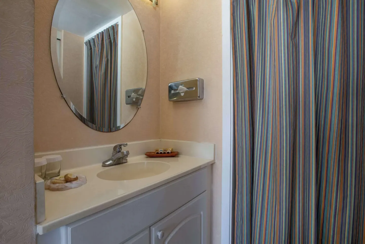 Deluxe Room bathroom vanity at Aqua Aloha Surf Waikiki with round mirror and striped shower curtain.