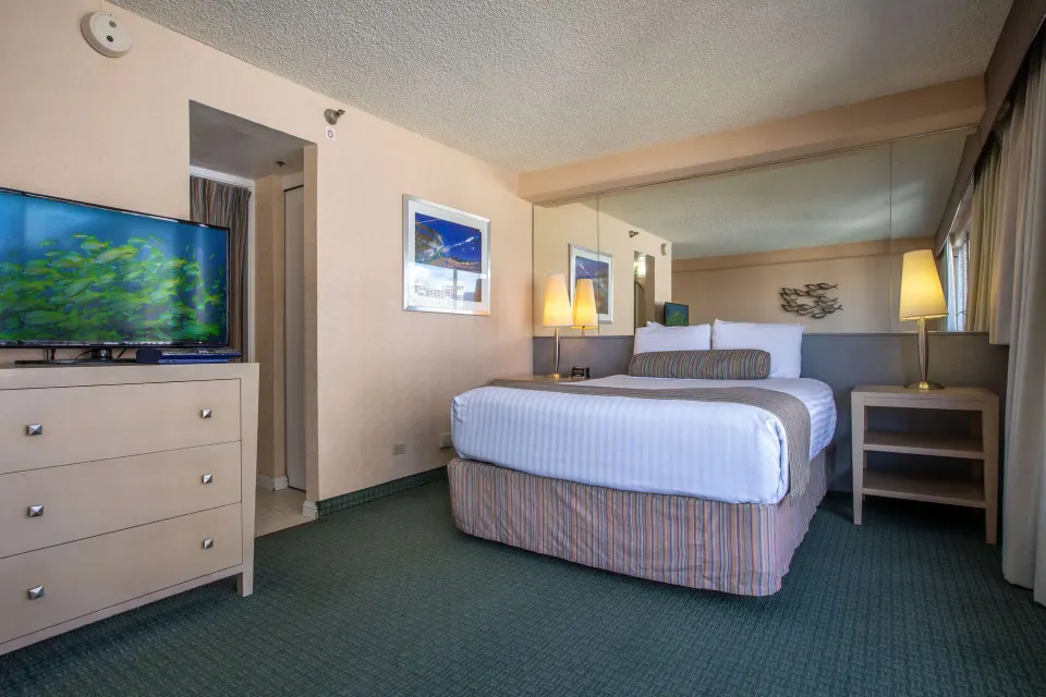 Deluxe Room king bed with dresser and TV at Aqua Aloha Surf Waikiki.