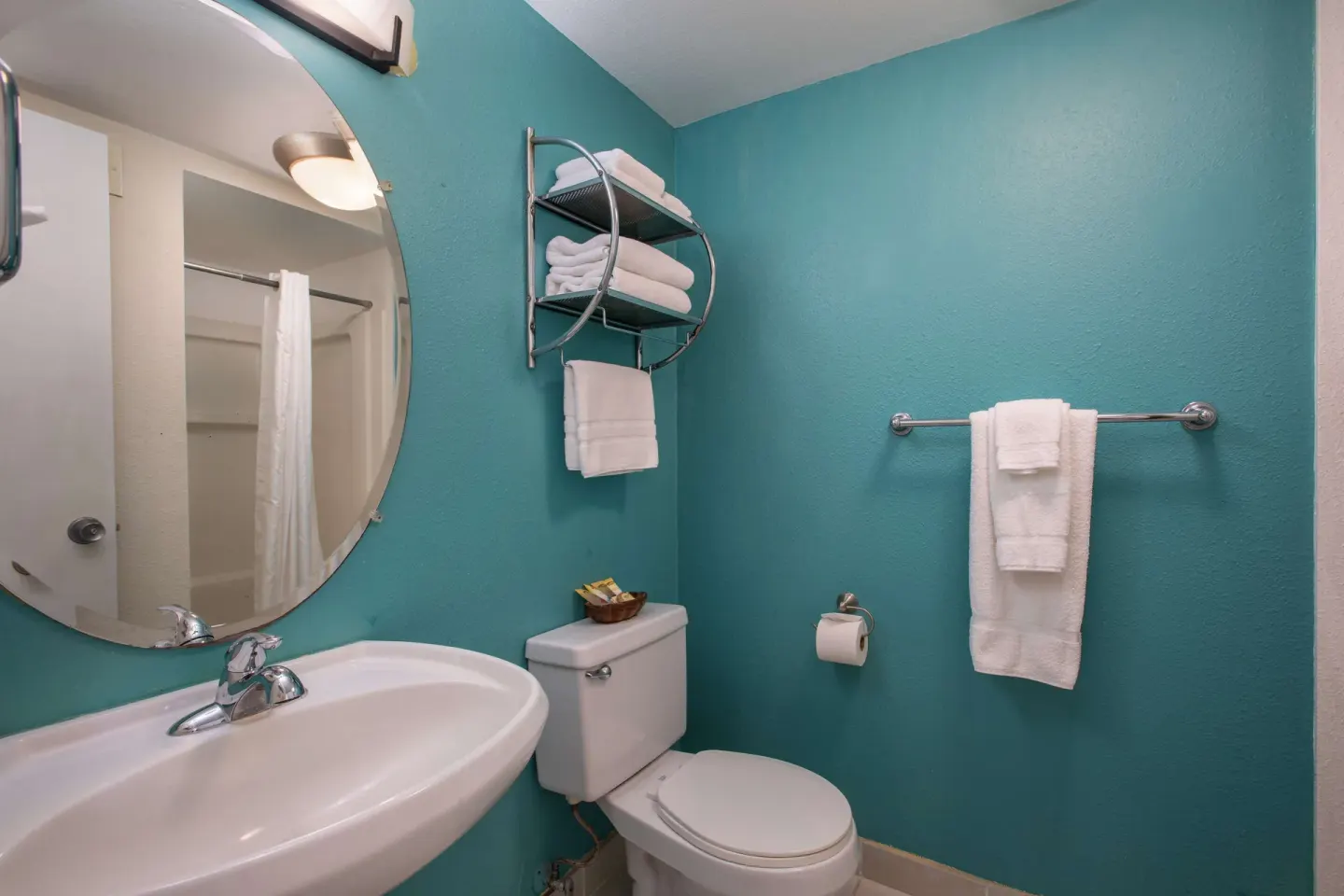 Moderate room bathroom with round mirror, sink, toilet, towels, and teal walls at Aqua Aloha Surf Waikiki.
