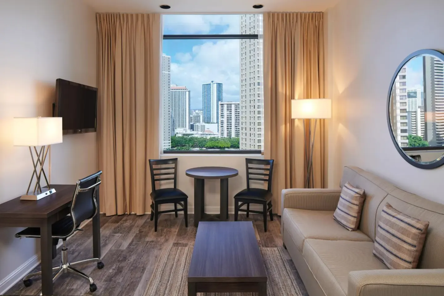 Living area with sofa, desk, dining table and city-view window at Aqua Palms Waikiki.
