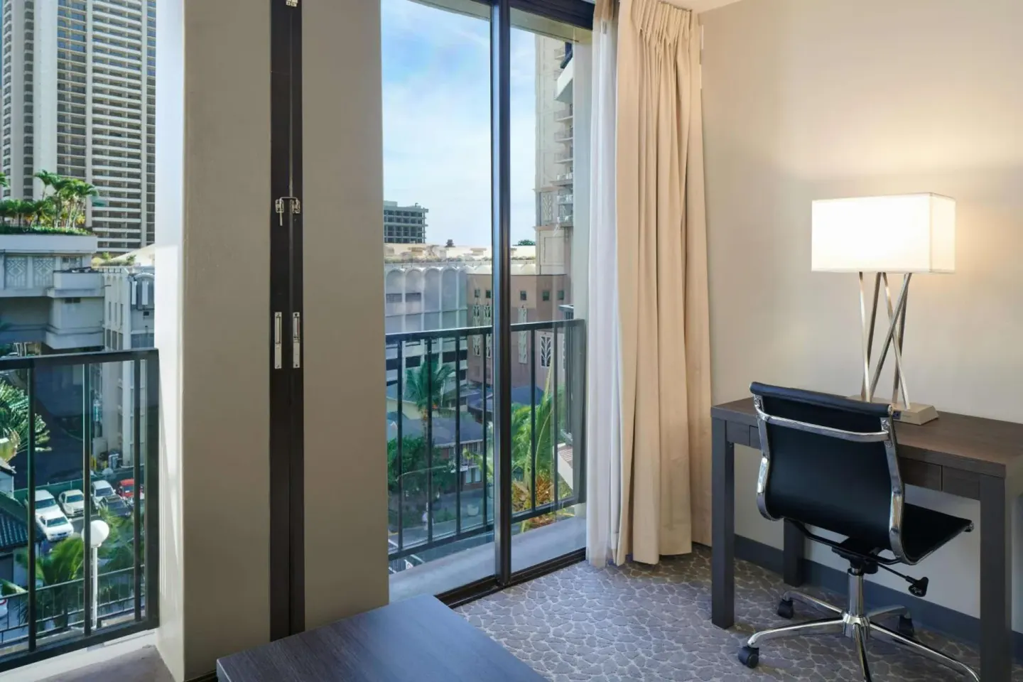 Guest room desk beside balcony doors with city buildings at Aqua Palms Waikiki.