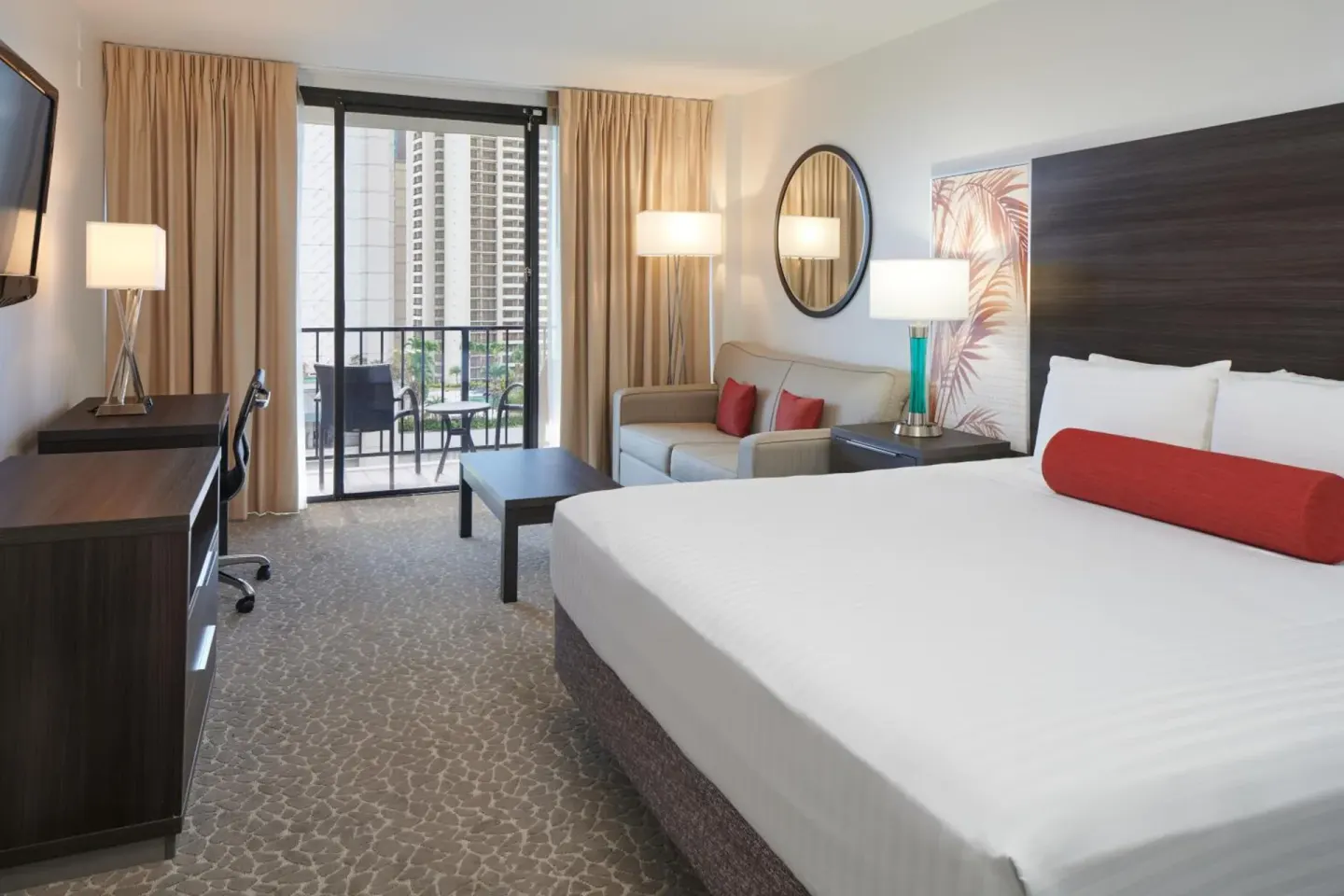 King bed, sofa, desk, and balcony doors in a guest room at Aqua Palms Waikiki.