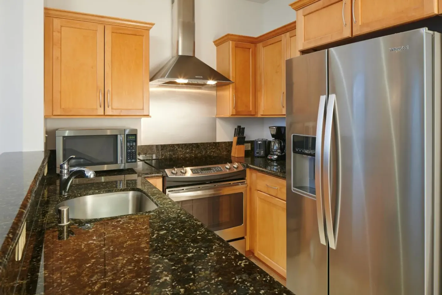 Guest suite kitchen with stainless appliances and wood cabinets at Aqua Palms Waikiki.