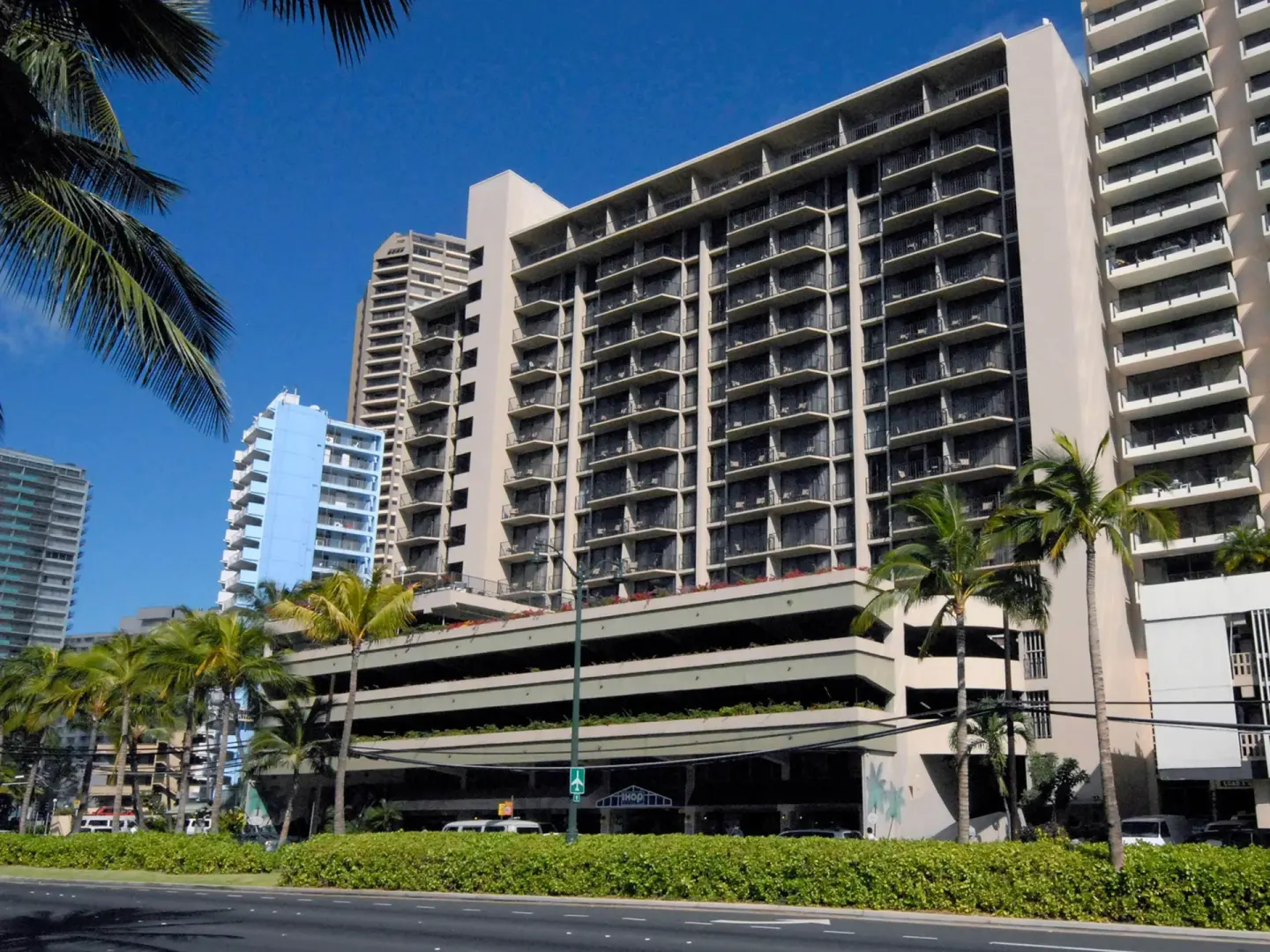 Tall hotel building with balconies and palm trees at Aqua Palms Waikiki.