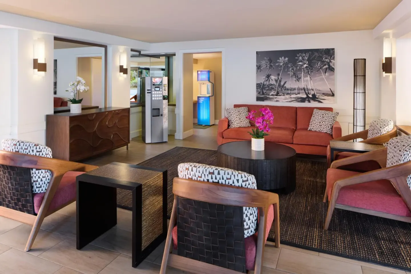 Lobby seating area with coral sofa, chairs and palm artwork at Aqua Palms Waikiki.