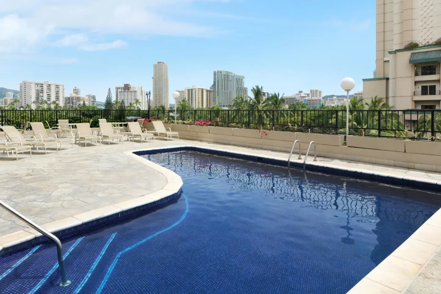 Outdoor pool with lounge chairs and city views at Aqua Palms Waikiki.