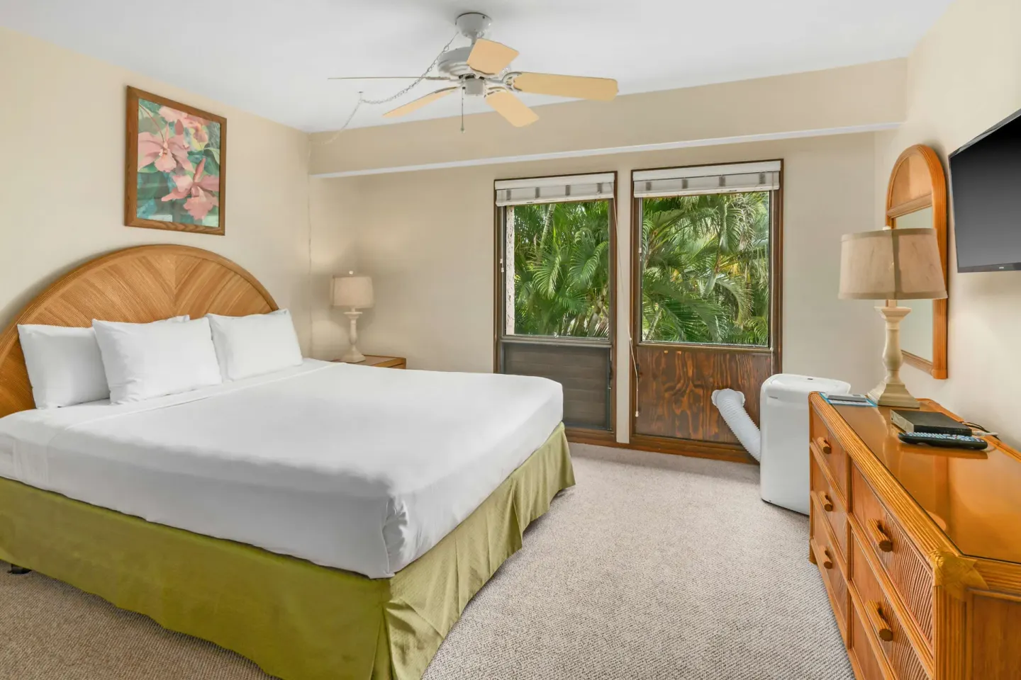 Bedroom with king bed, dresser, TV, and leafy window view at Aston at Poipu Kai.