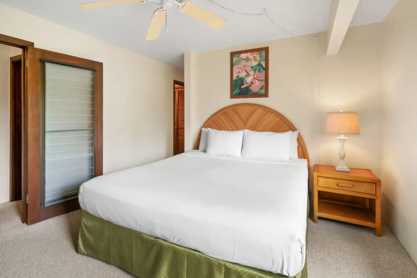 King bedroom with wood headboard, bedside lamp, and louvered door at Aston at Poipu Kai.