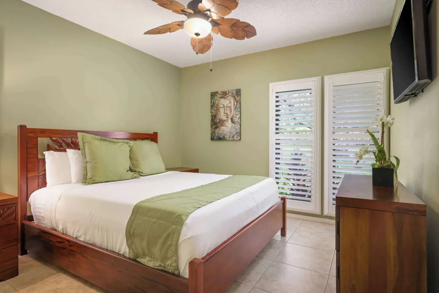 Compact bedroom with wood bed, shutters, dresser, and wall-mounted TV at Aston at Poipu Kai.