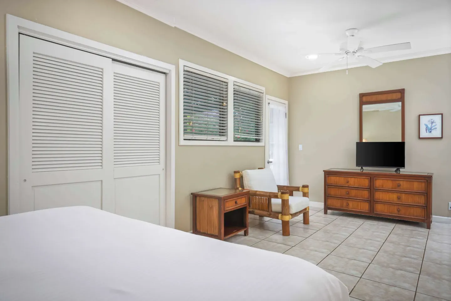 Guest bedroom with bed, dresser, TV and lounge chair at Aston at Poipu Kai.