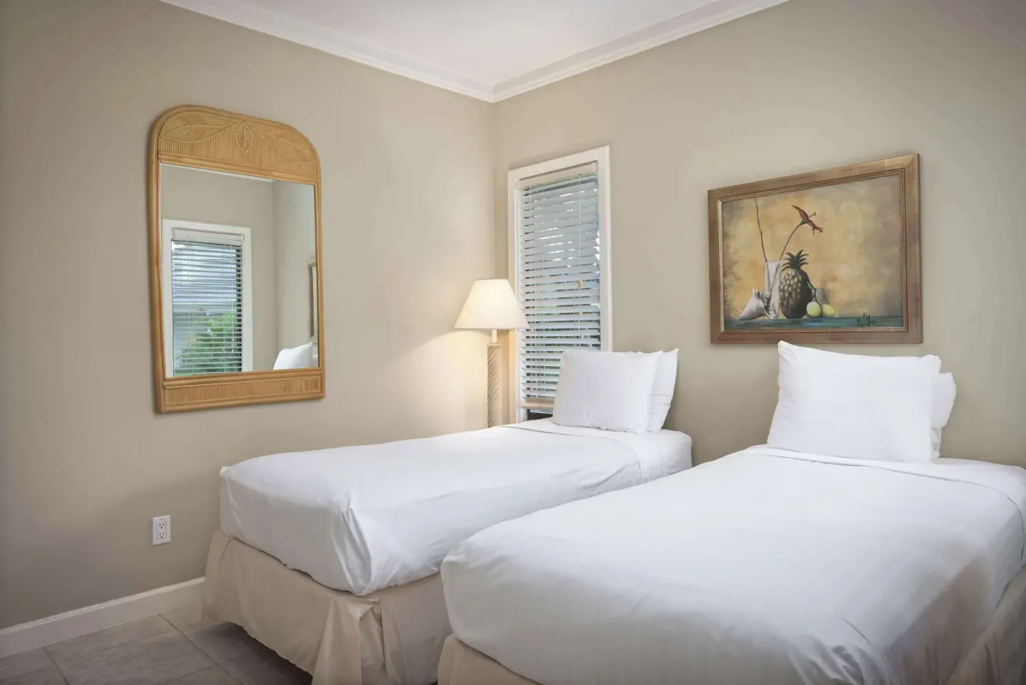 Guest bedroom with two twin beds, wall mirror and table lamp at Aston at Poipu Kai.