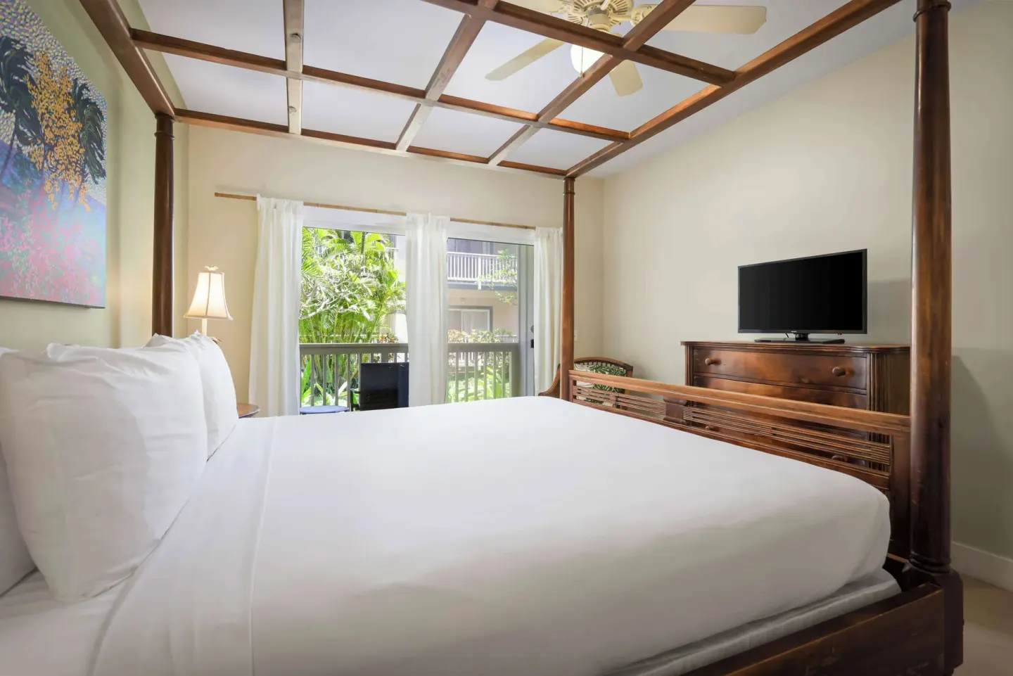 King bedroom with four-poster bed, balcony doors, and dresser at Aston at Poipu Kai.