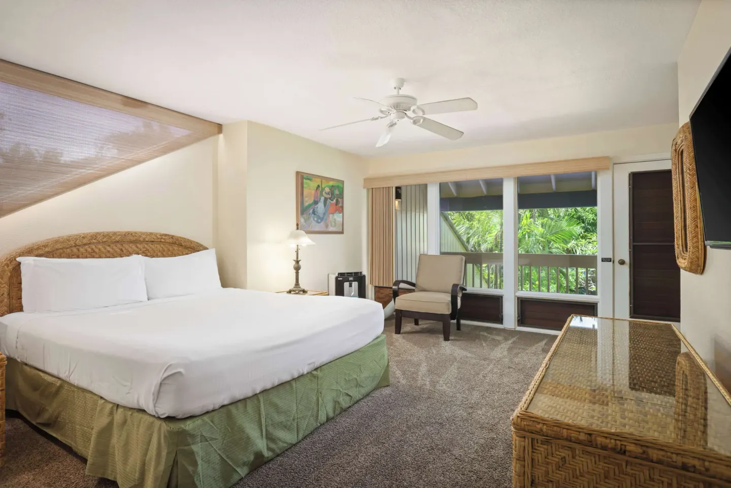 King bedroom with wicker furniture, balcony doors, and sitting chair at Aston at Poipu Kai.