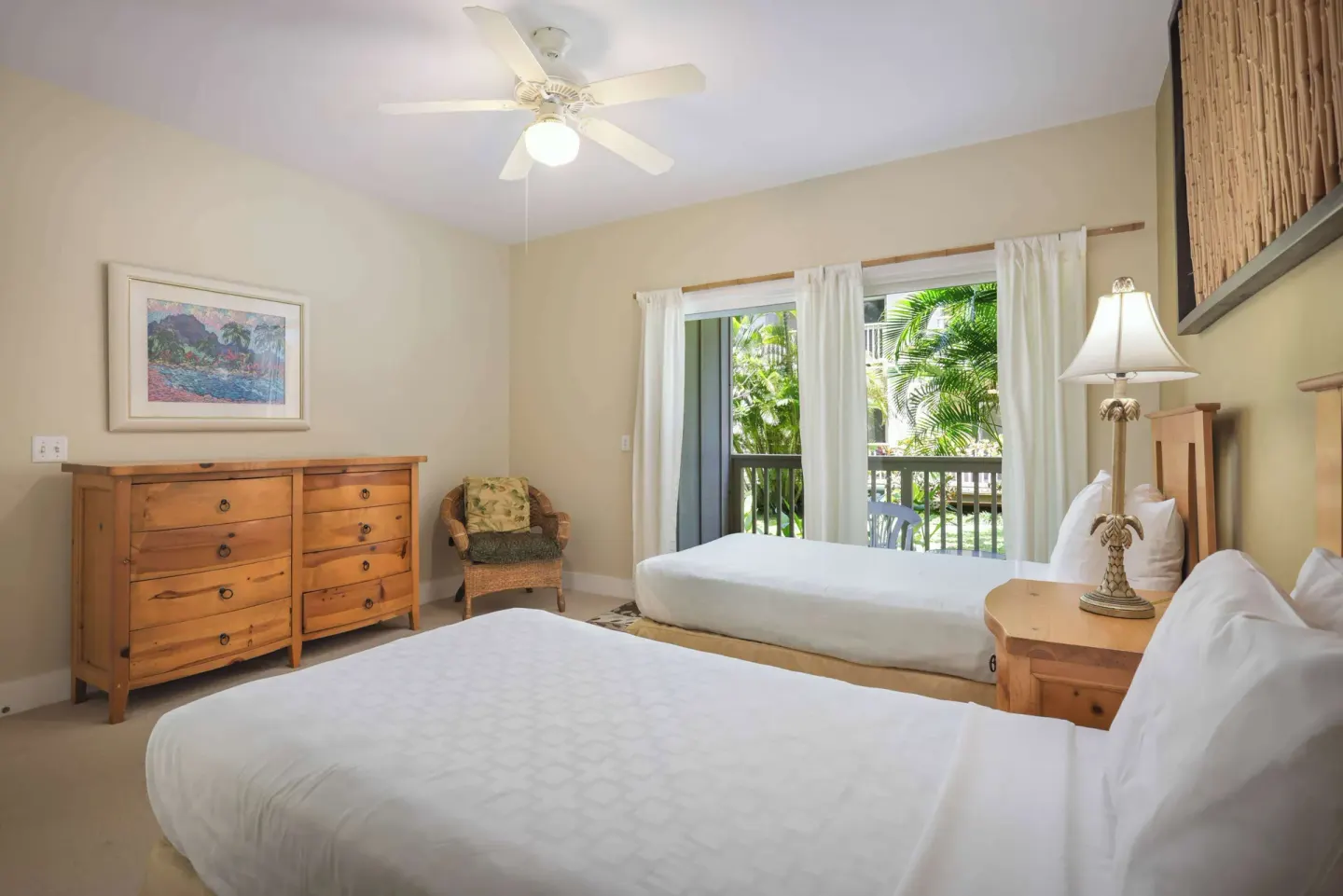 Twin bedroom with wood dressers, balcony doors, and tropical greenery at Aston at Poipu Kai.