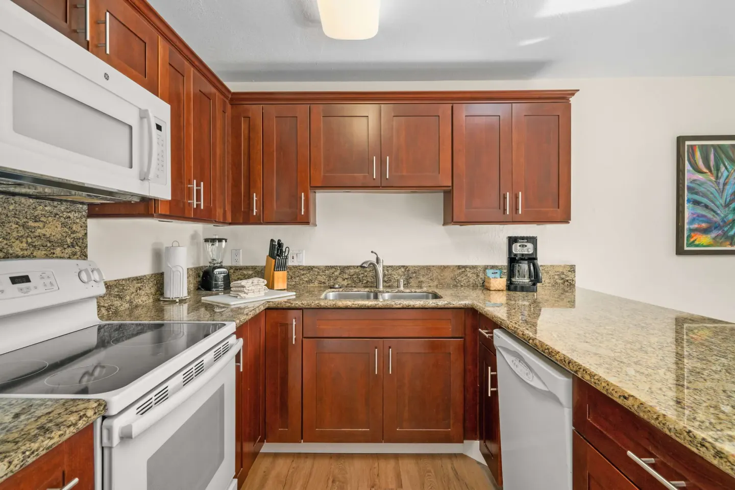 Kitchen with dark wood cabinets, granite counters, white stove, and dishwasher at Aston at Poipu Kai.