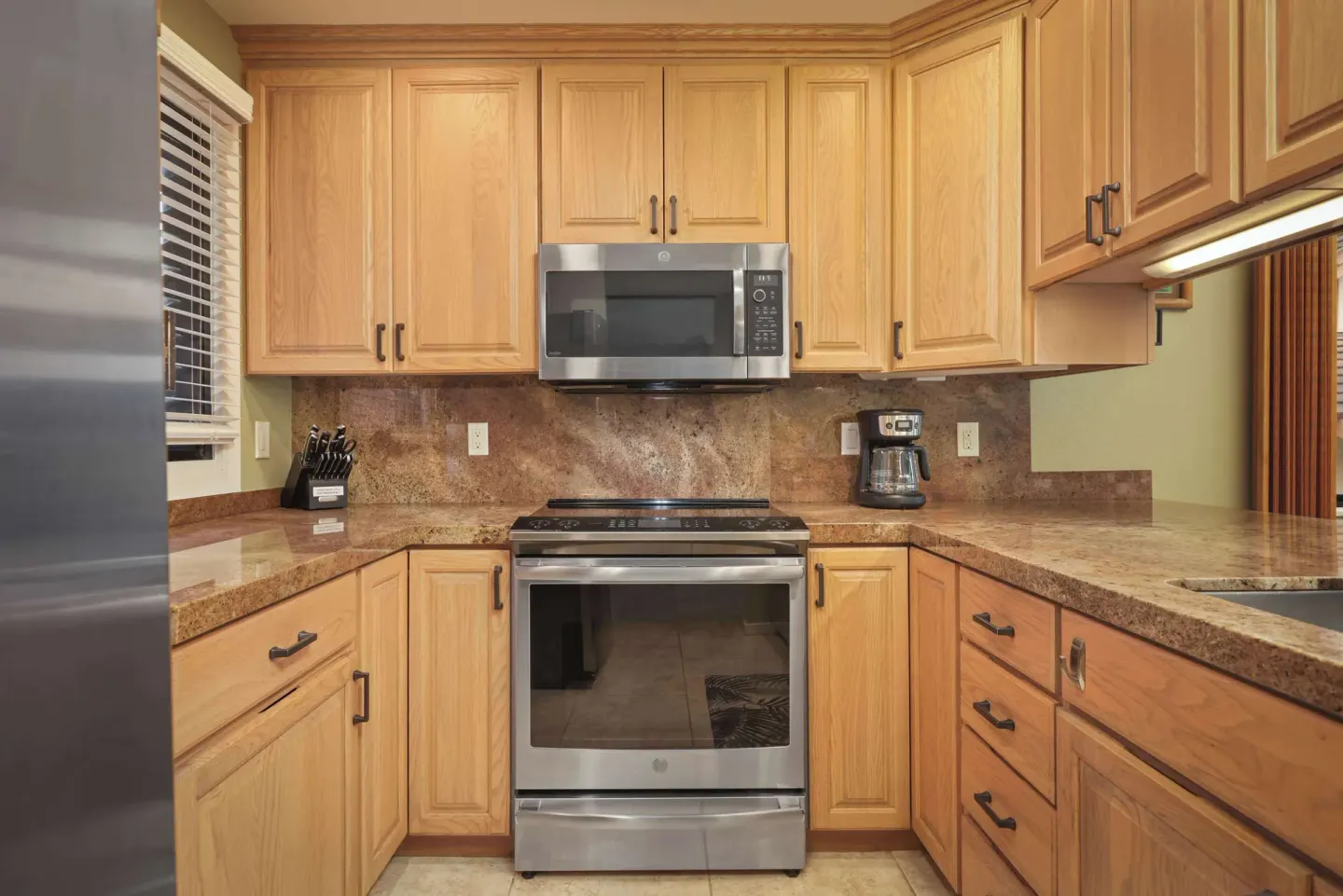 Kitchen with light wood cabinets, stainless range, microwave, and coffee maker at Aston at Poipu Kai.