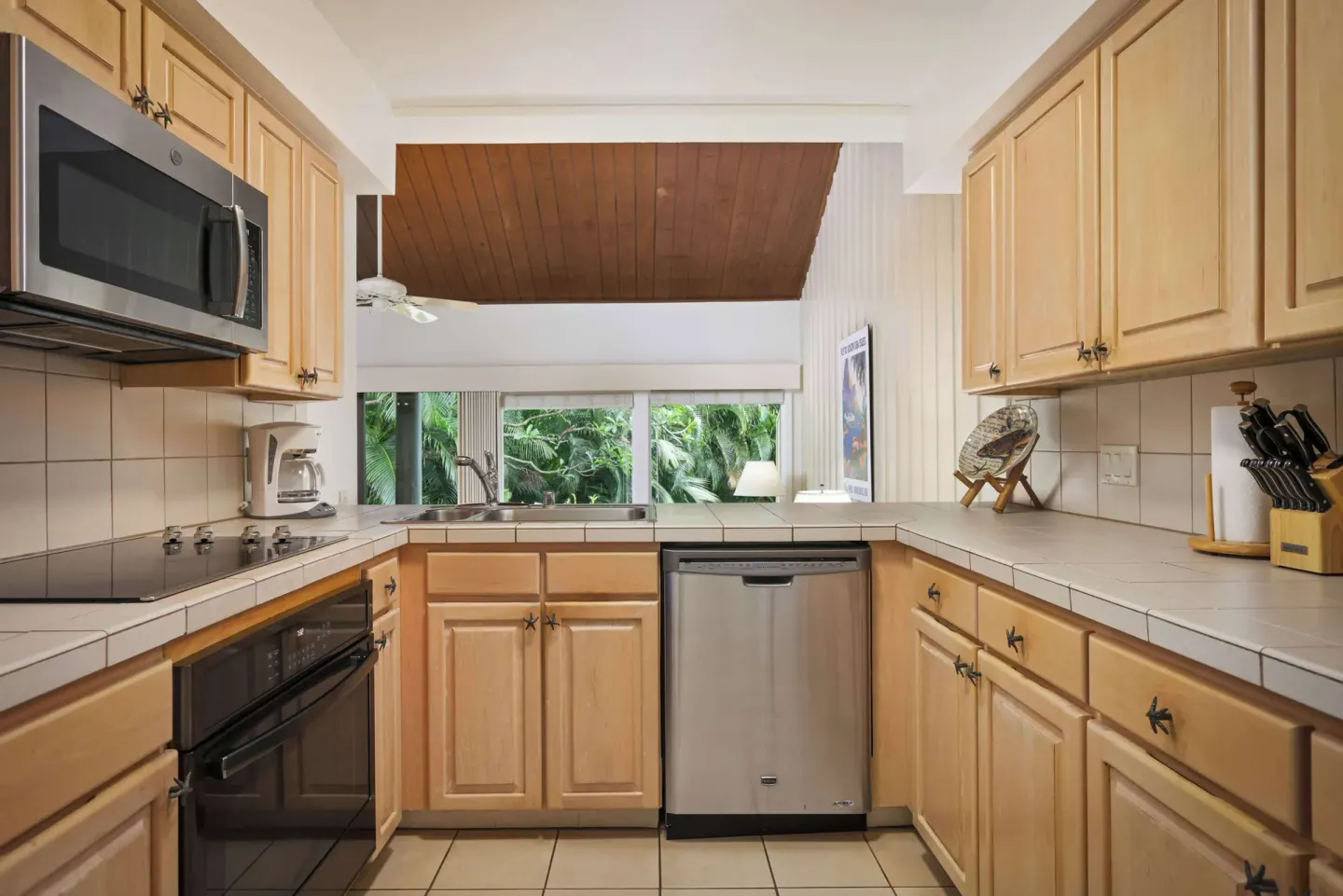Kitchen with wood cabinets, tile counters, dishwasher, and microwave at Aston at Poipu Kai.