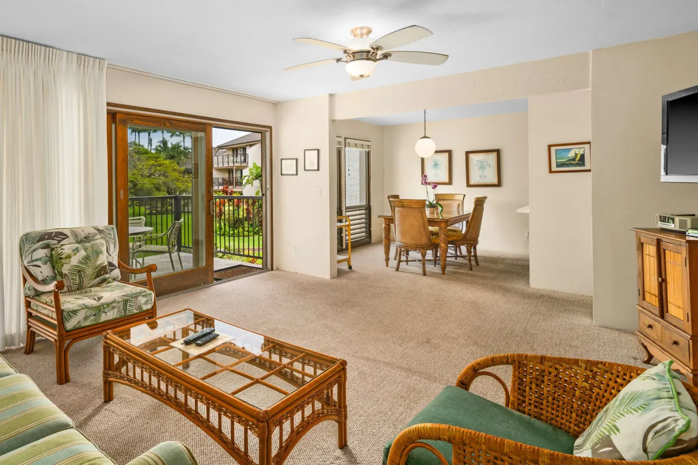 Living and dining area with balcony doors and wicker seating at Aston at Poipu Kai.