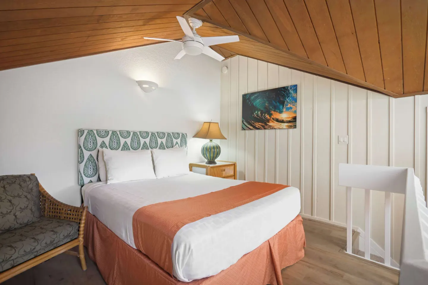 Loft bedroom with queen bed, wicker chair, and vaulted wood ceiling at Aston at Poipu Kai.