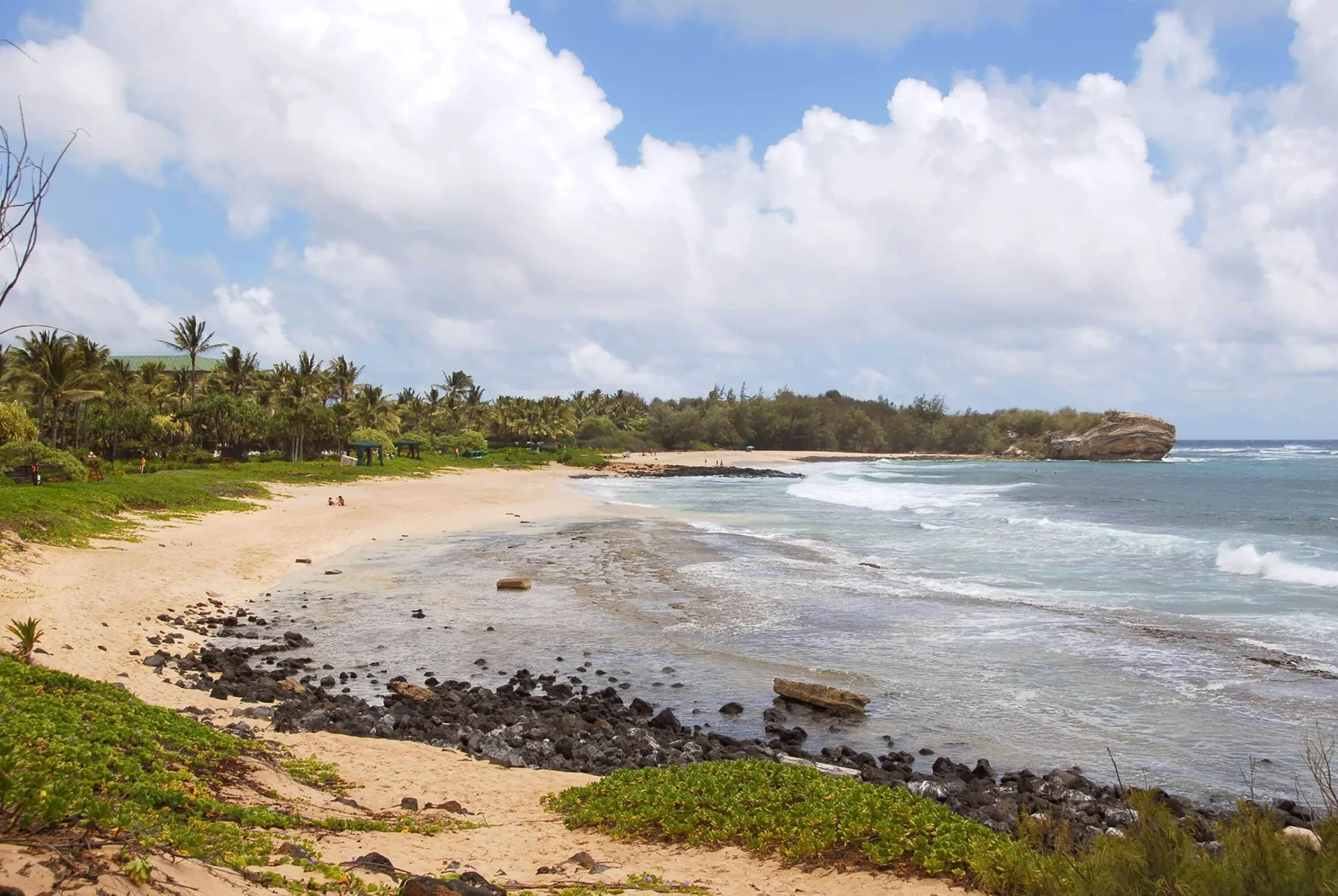 Sandy beach with rocks, surf, and palms near Aston at Poipu Kai.
