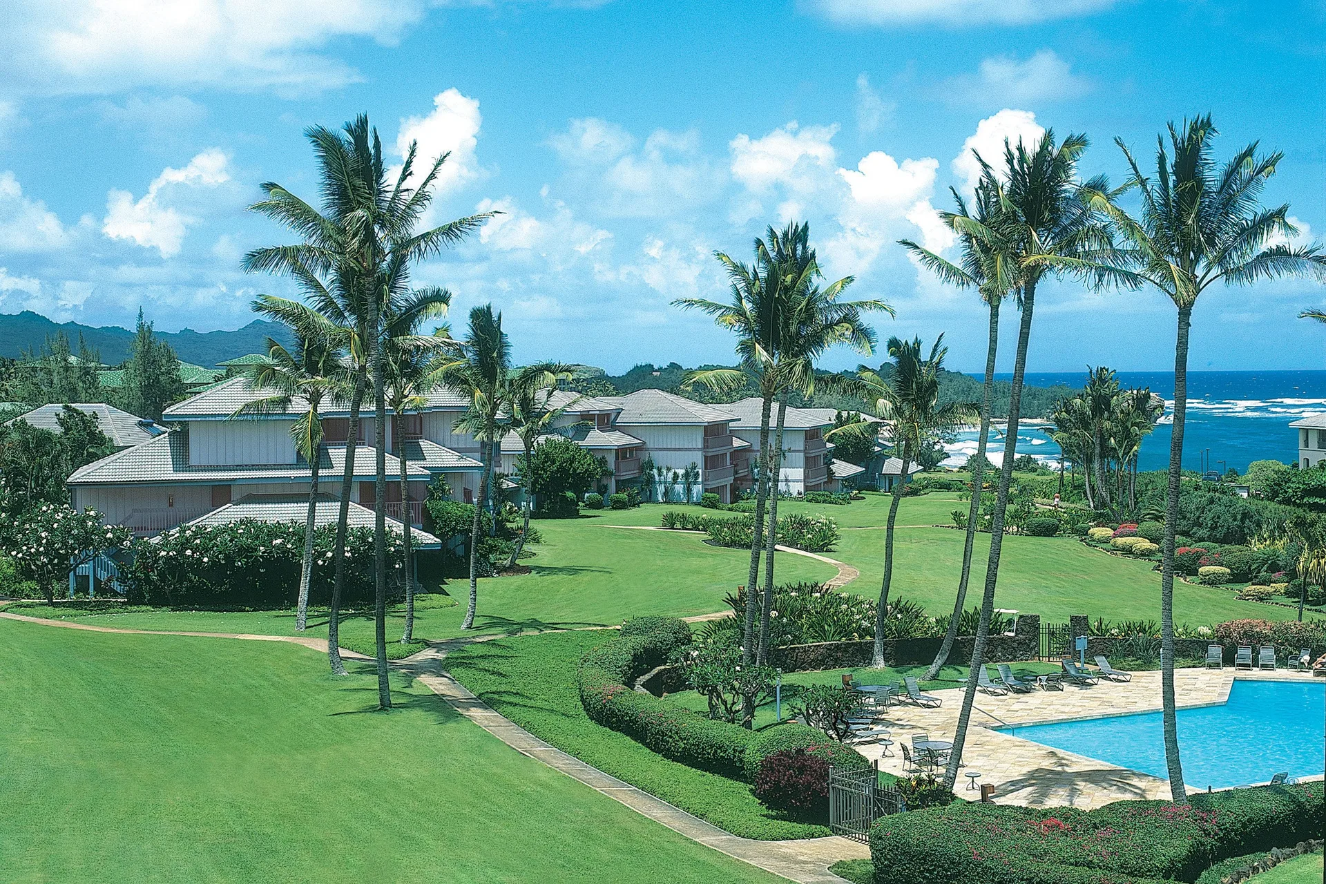 Pool, lawns, palms, and ocean beyond the buildings at Aston at Poipu Kai.