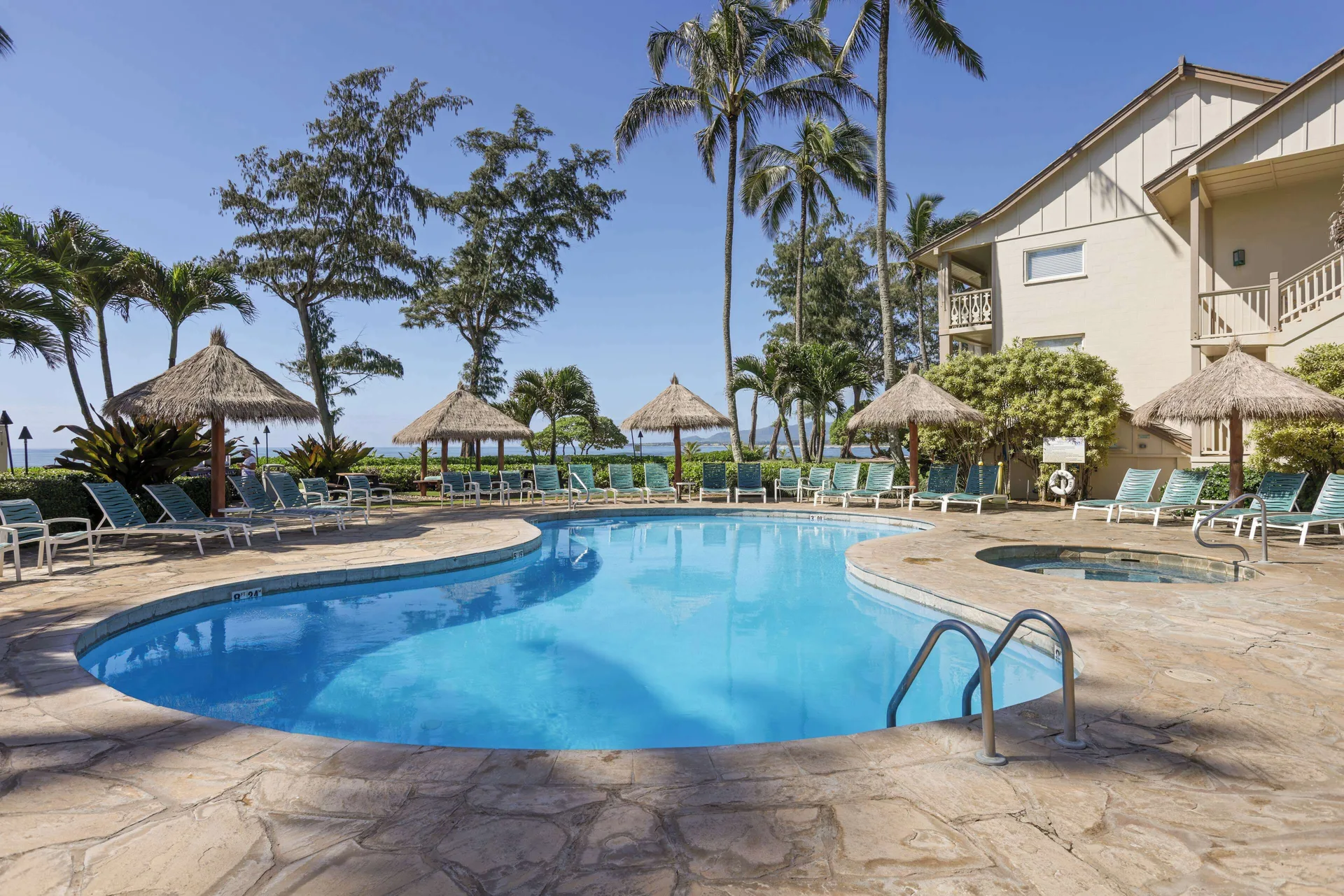 Curved outdoor pool with lounge chairs and palms at Aston Islander on the Beach.
